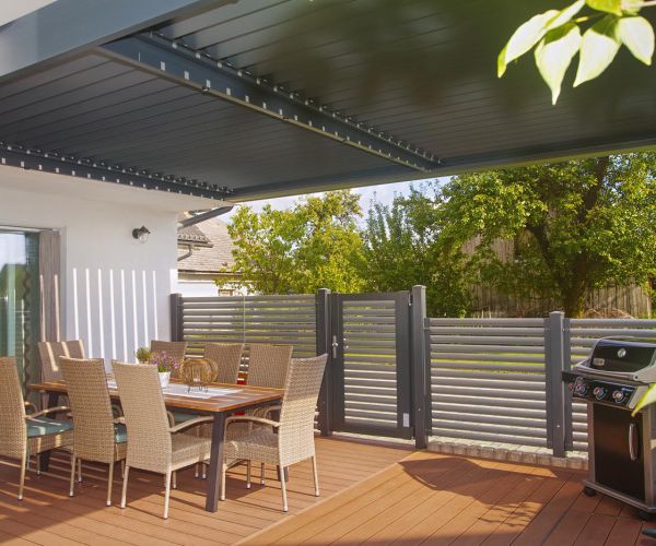 Elegantna bioklimatska pergola Misteral, nameščena na prostorni terasi ob vrtu, z usmerjenimi lamelami za optimalno zaščito.