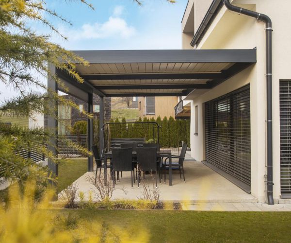 Sodobna bioklimatska pergola Misteral z avtomatskimi lamelami, nameščena na prostorni terasi, za uživanje na prostem v vsakem vremenu.